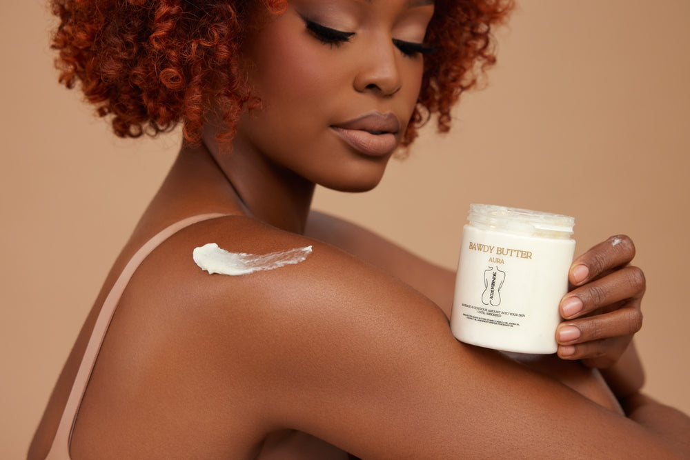 Woman applying body butter to her shoulder against a beige background